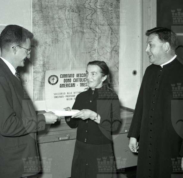 Trieste, Monsignor Alfredo Bottizer con Maria Copich, la prima profuga giuliana che ottenne il visto per gli Stati Uniti d’America e Mister Dick Haising, ufficiale americano per l’emigrazione. Tratto da "Il Piccolo", 11.11.1954. Fotografia da: Palazzo Gopcevich; Fototeca dei Civici Musei di Storia ed Arte, Trieste; Archivio Giornalfoto